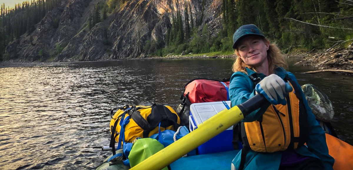 Woman in raft with cliff and river in background