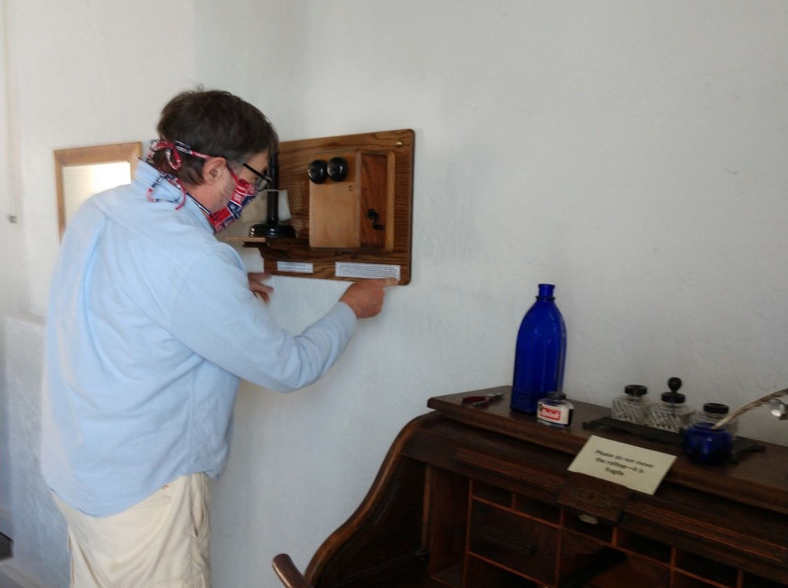 a man installs a candestick-style telephone onto a wall