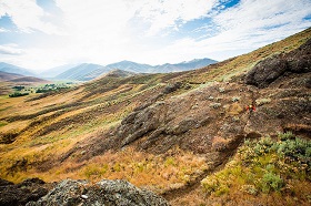 Treeless hills with green vegetation and dark grey rocks under a partially cloudy sky. Croy Creek Recreation Area, Idaho.