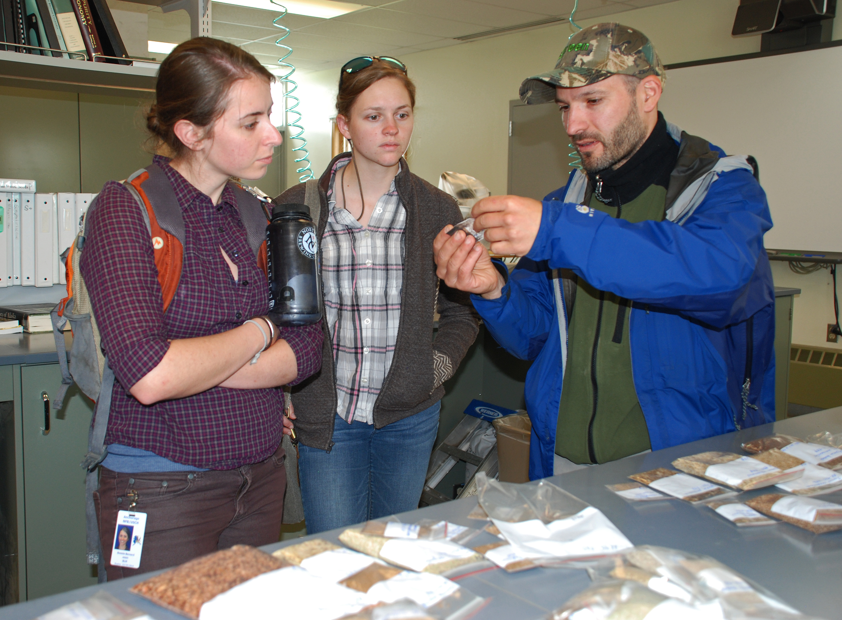 Seeds of Success interns Charlotte Crowder and Bonnie Bernard examine seed plugs held up by seed program manager Lyubomir Mahlev in the Plants Material Center.