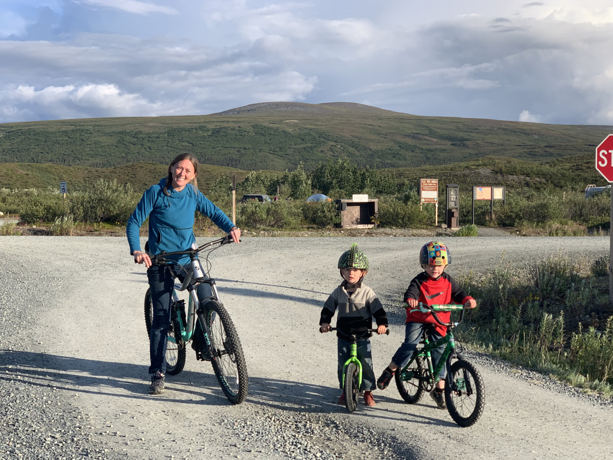 A woman and two young boys pose for a picture on their bicycles.