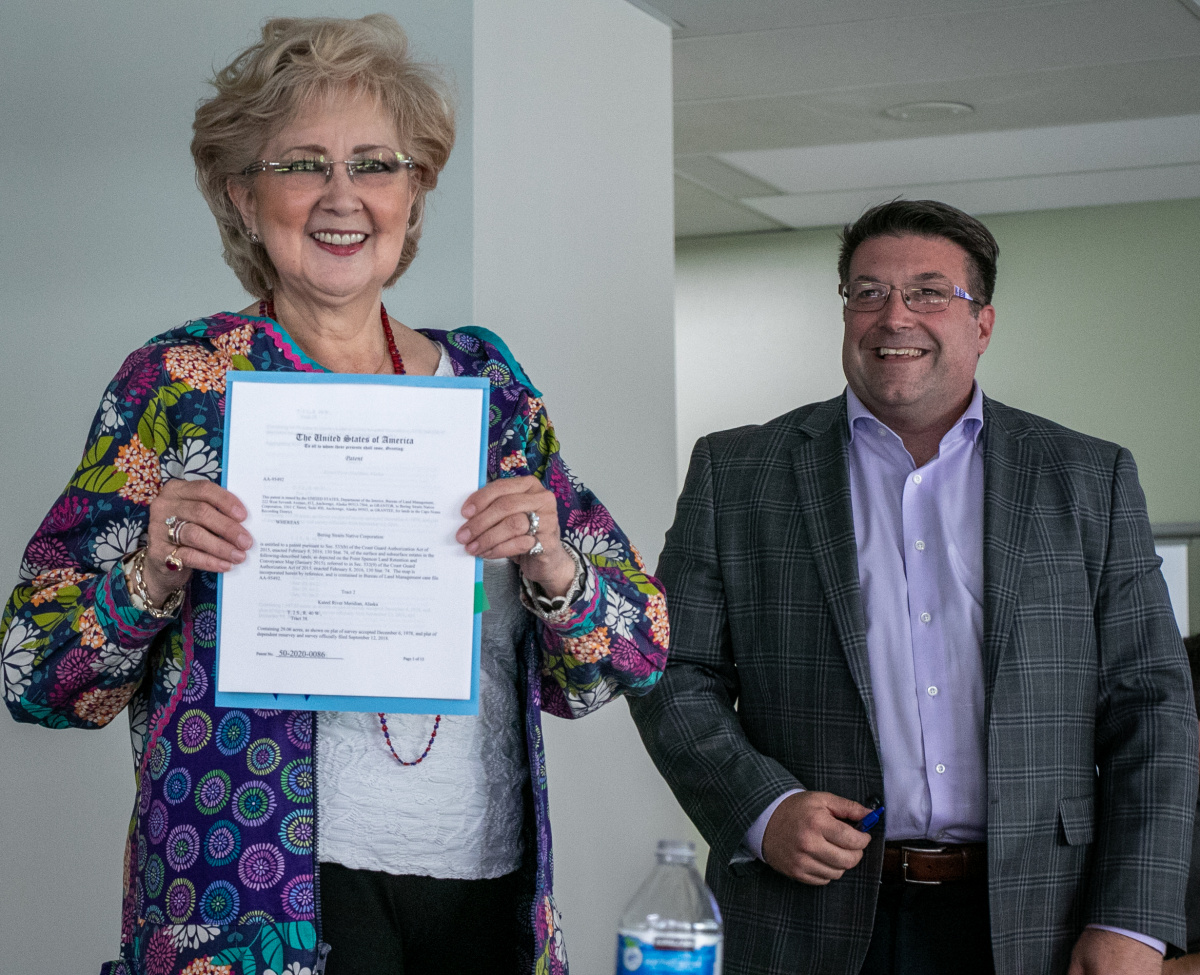 A woman holding a piece of paper with a man smiling behind her