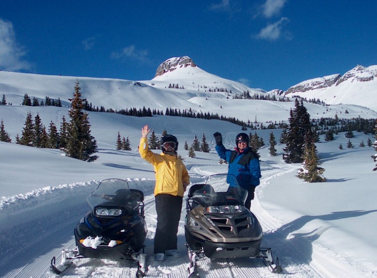 two individuals standing next to snowmobiles