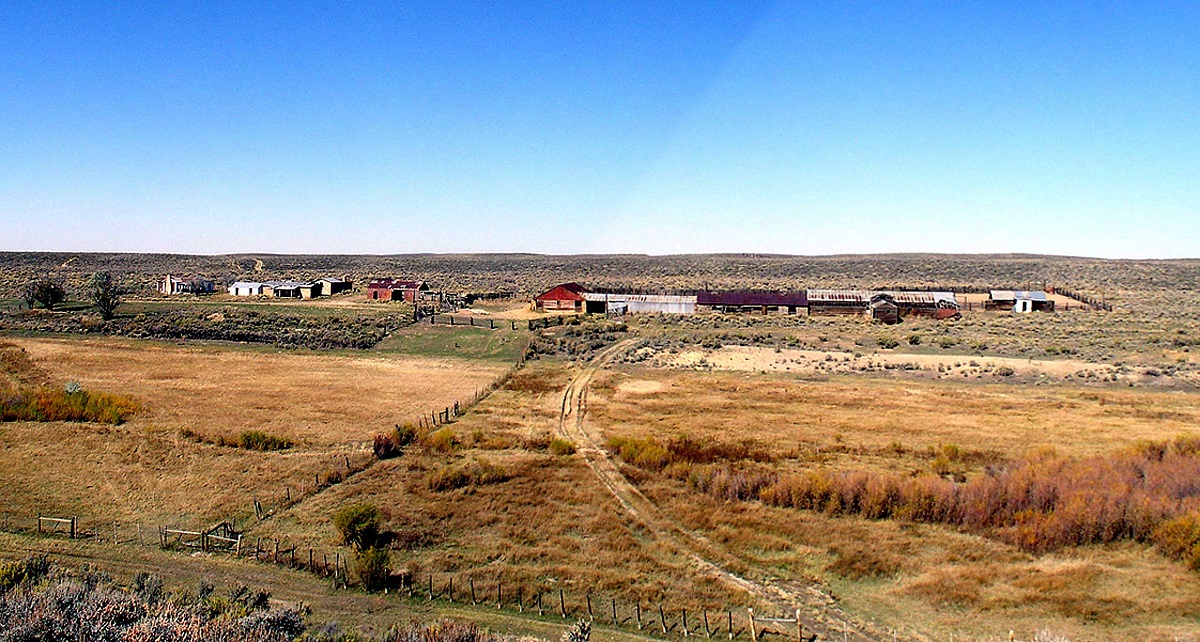 A distance view of about a dozen old ranch buildings surrounded by prairie.