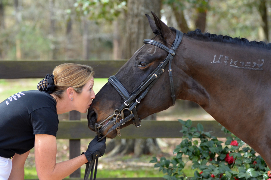 Woman with hands on horse's face. 