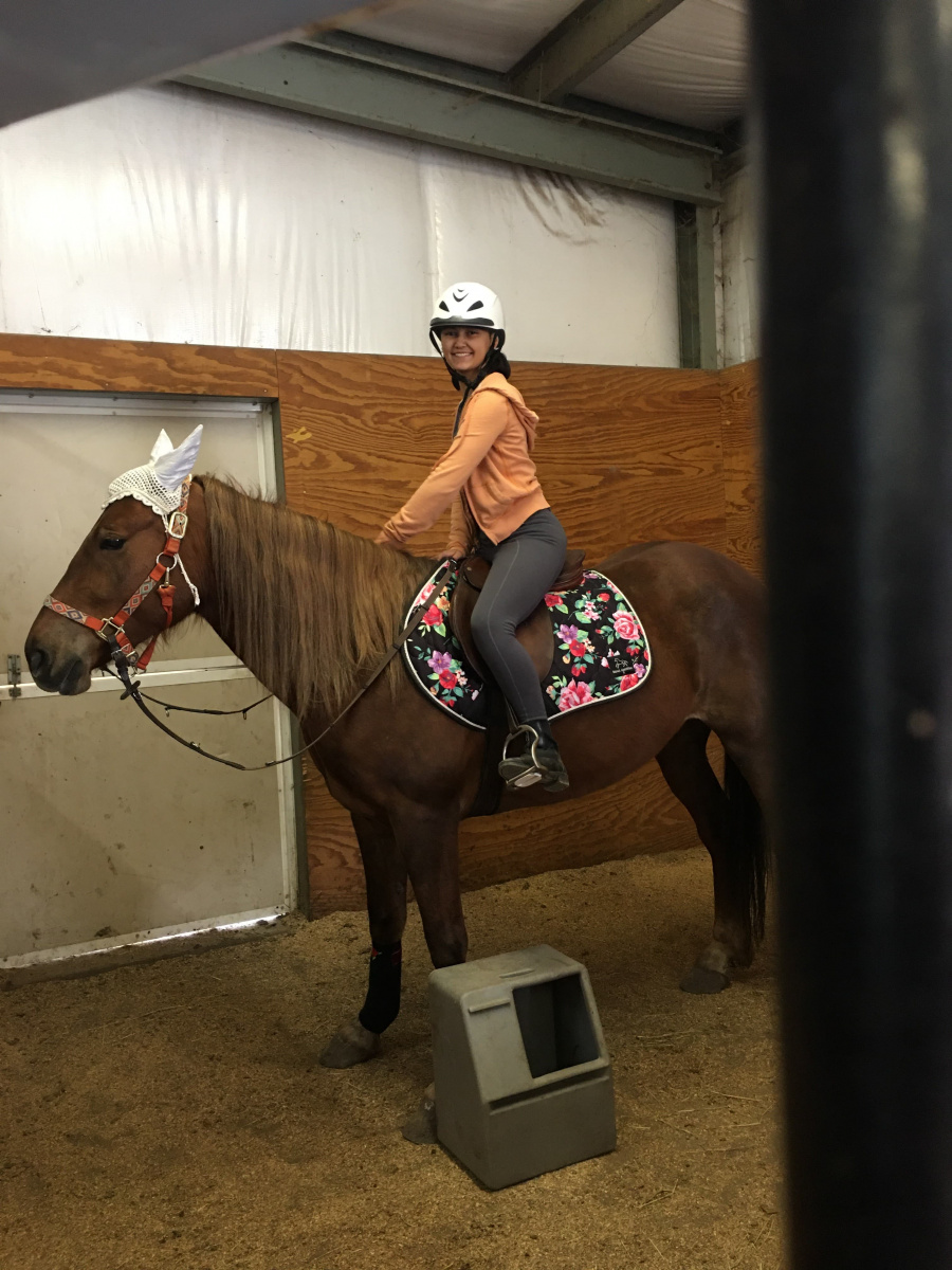 A woman indoors riding a horse with a hat. 