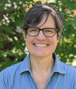 headshot of woman with short dark hair, glasses and a blue shirt