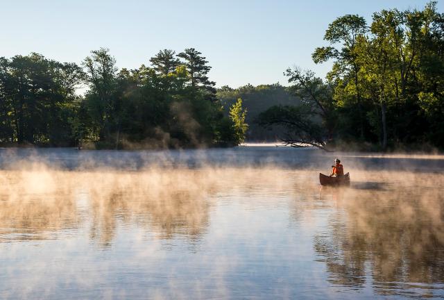 Fisherman wearing orange life jacket and tan hat at sunset with a blanket of fog surrounding the boat.