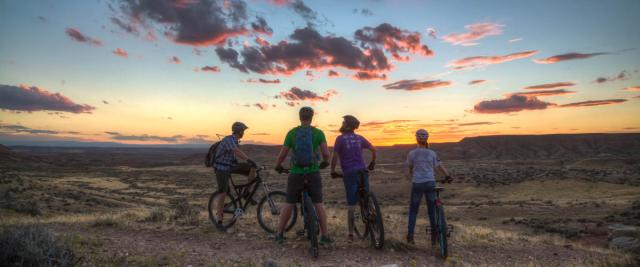 Four bike riders in the Utah desert facing a sunset