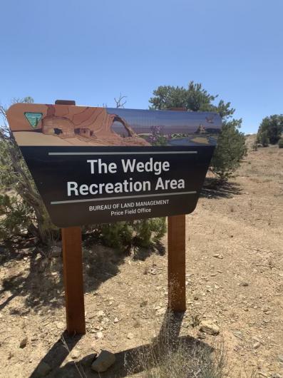 A BLM Portal sign with a desert landscape at the Wedge Overlook with dirt and shrubs surrounding it.