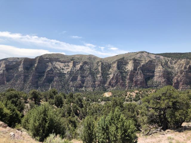 Sandstone Cliffs with the blue sky and clouds. Sagebrush clumps dot the landscape. Photo by Ray Kelsey.