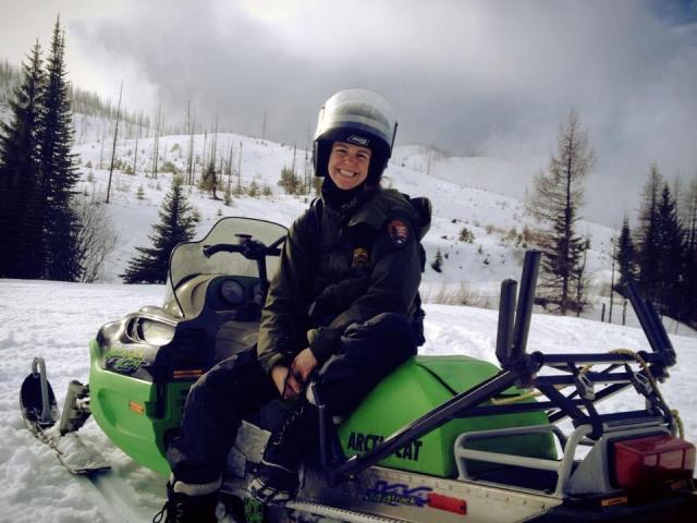 Law enforcement ranger sits on snowmobile in backcountry