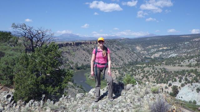 Erin wearing a hat standing on rocks with a river below her