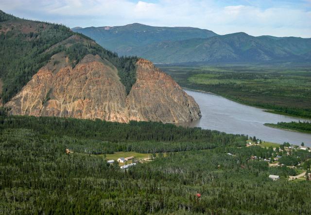 A grassy meadow sits at the base of high cliffs next to a river and small town.