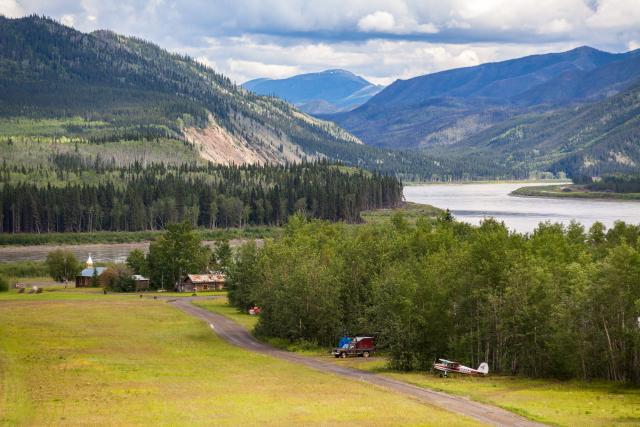 A grassy field leads toward a river in front of mountains.