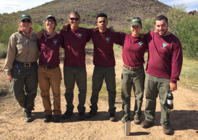 Six field school students stand in a clearing in the desert with a mountain in the background