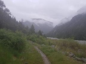 A path along the river. Low cards cover the mountains in the distance.