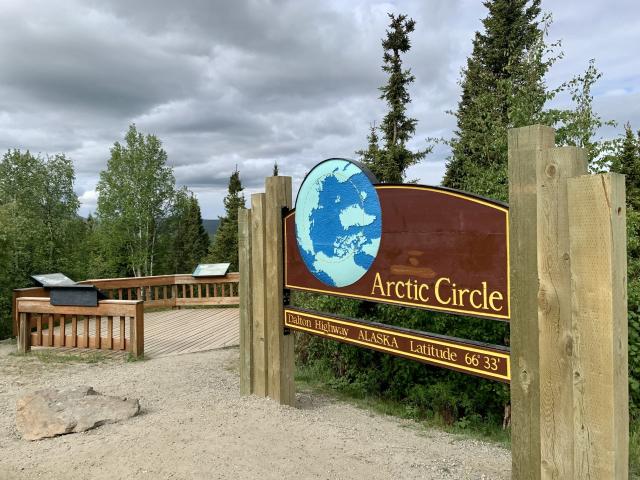 A wooden sign for the Arctic Circle, Dalton Highway, Alaska, Latitude 66° 33’.  Depicts north pole of the earth with the arctic circle shown in a dashed line. 