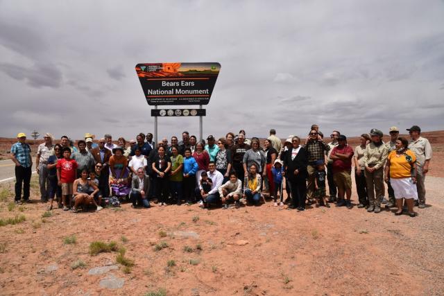 Tribal leaders and partners gather with BLM and U.S. Forest Service employees underneath the Bears Ears National Monument sign.