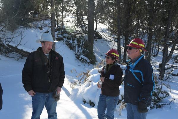 Jennifer Walker (center) and former Buffalo Field Manager Duane Spencer (right) discuss a restoration project implemented in collaboration with an adjacent landowner. They are standing with hard hats on in the snow surrounded by trees. 