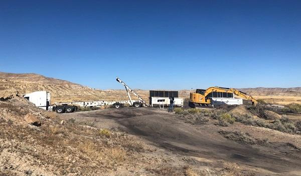 A yellow crane on the right and a truck on the left. Hills in the background. 