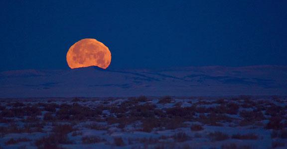 A full moon rises over snowy sagebrush steppe