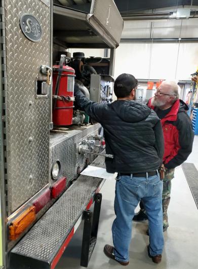 Two individuals standing in front of a fire truck looking over the equipment.