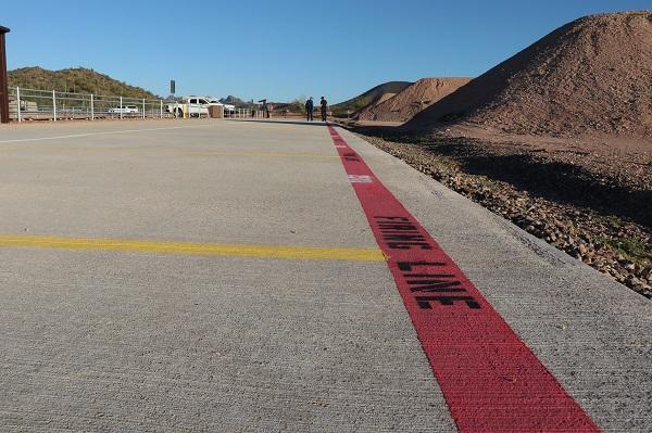 concrete shooting platform with a painted red firing line running across it. Two people are standing in the distance. 