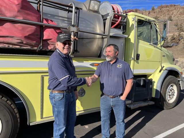 Nathan shakes hands with Richard Shaffer, Wheeler County Fire Coordinator, after signing the final paperwork to transfer the water tender to Wheeler County RFPA