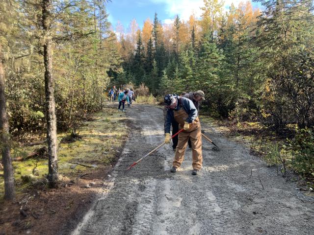 Man with rake spreading gravel on trail surface