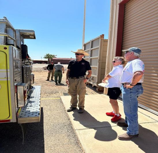 Three people standing off to the side of a bright yellow fire engine.