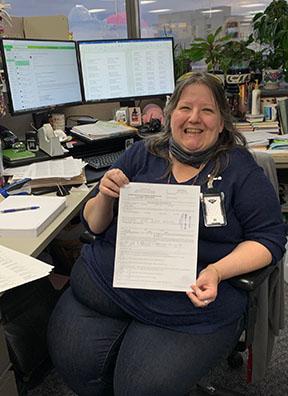 A person sits at a desk smiling holding an application.