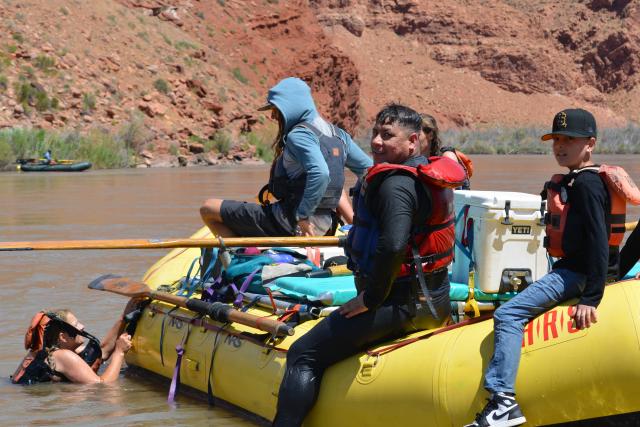 A swimmer about to get back on the yellow raft after others already came onboard in the river.