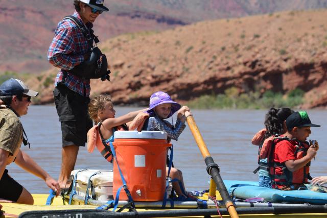 The guide reaches youth how to row the yellow river raft in calm waters.