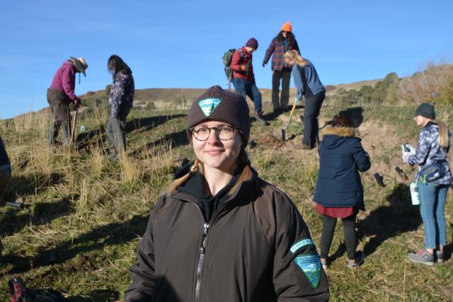 A person looking forward with a group of people gathered on the hill behind them. 