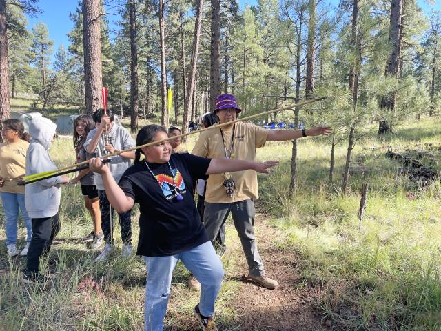 Yevingkarere Camp Elders teach Paiute youth traditional skills in a forested area.