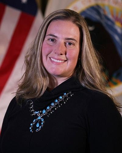 person with long hair wearing a black shirt and silver necklace posing in front of the American flag