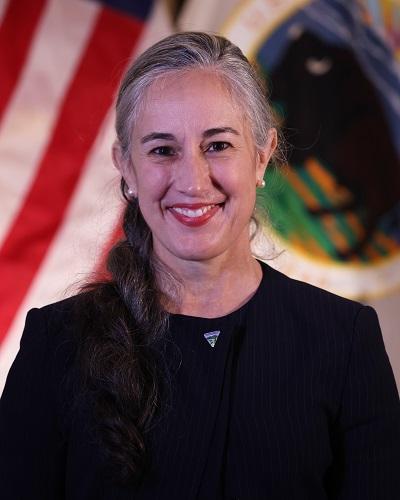 person with long hair wearing a black shirt posing in front of the American flag