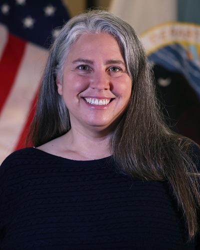 person with long hair wearing a black shirt posing in front of the American flag