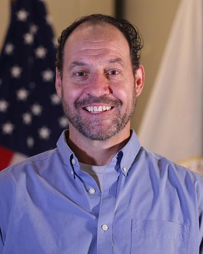 person with short hair wearing a collared shirt posing in front of the American flag