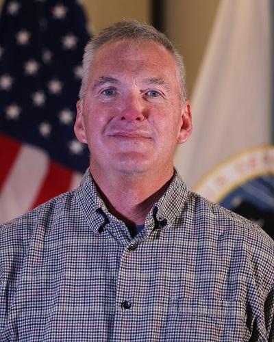 person with short hair wearing a collared shirt posing in front of the American flag