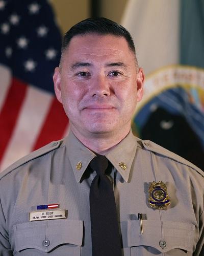 person in a uniform with badge and tie posing in front of an American flag