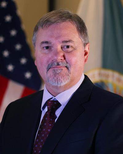 person with short hair wearing a tie posing in front of the American flag