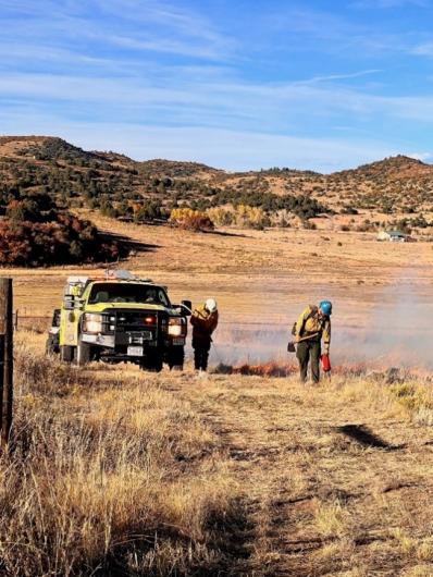 A fire engine and several people conducting a prescribed burn. 