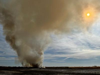 Plume of smoke rising over the sun in the desert.