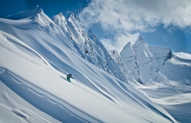 Image of a skier coming down a snowy steep mountain slope.