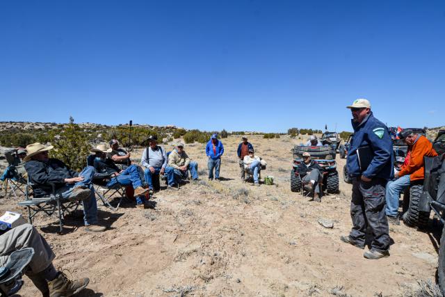 A person presenting a discussion outside by a group of OHVs on the landscape.