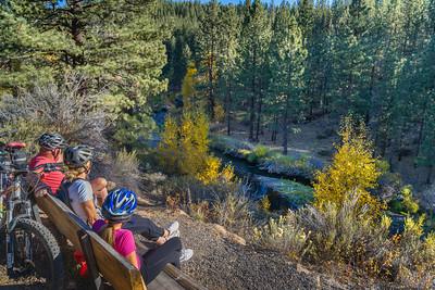 Three people sitting on a bench overlooking a river.