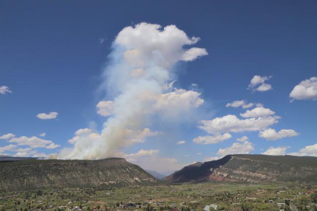 A smoke column rises from a mountain overlooking a town