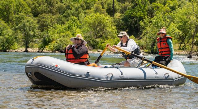 three people with life jackets in a white water raft.